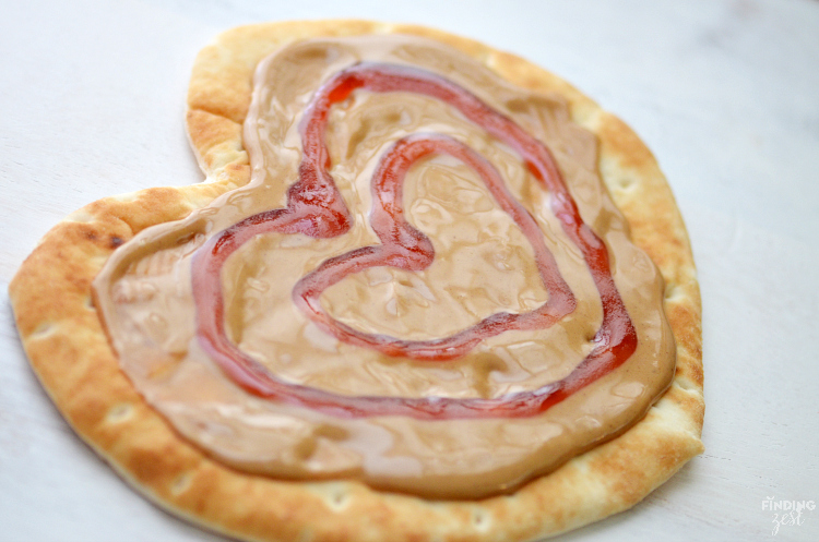 Show someone you care with this Peanut Butter and Jelly Heart Flatbread! Serve with apple heart cutouts and cold milk for the perfect lunch on Valentine's Day, back to school or any time of year.