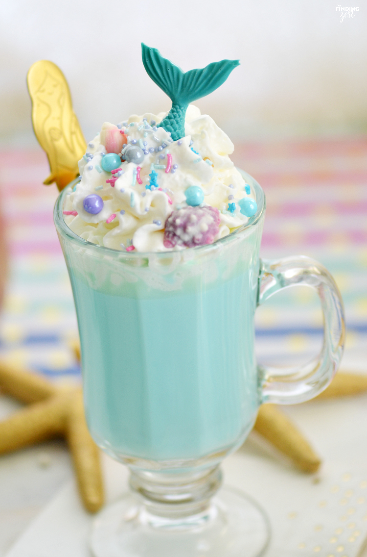 Make a cup of cocoa extraordinary with this Blue Mermaid Magic Hot Chocolate recipe You have to try it! Using homemade white hot chocolate, this delicious blue drink is loaded with fun sprinkles, whipped cream and topped with a chocolate mermaid tail. Mermaid lovers of all ages will go nuts for this hot mermaid drink! Perfect to serve guests at a mermaid birthday party. The mermaid spoons also make great party favors.