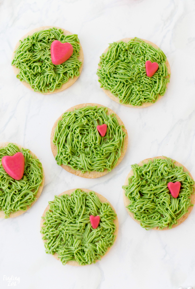 Everyone will love these adorable Grinch Cookies to celebrate the beloved Dr. Seuss character during the holiday season! This sugar cookie features green frosting to look like fur and three sizes of fondant hearts to represent his heart growing three sizes that one fateful day. These Grinch-inspired treats are super easy and fun for all ages to make and enjoy!