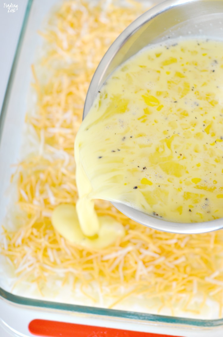 Pouring eggs over hash browns and cheese before baking