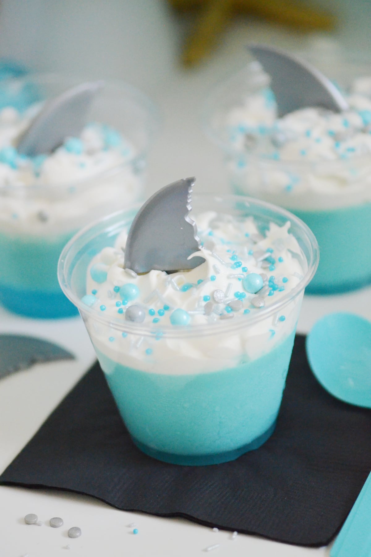 Get ready to dive into some fun with this shark dessert! Kids will love this baby shark jello complete with silver shark fin, fluffy white waves and fun sprinkles! This is an easy dessert for any baby shark birthday party.