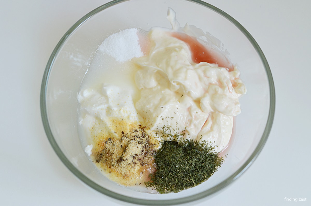 Creamy cucumber dressing in a bowl with mayo, sour cream, dill, garlic, vinegar, sugar
