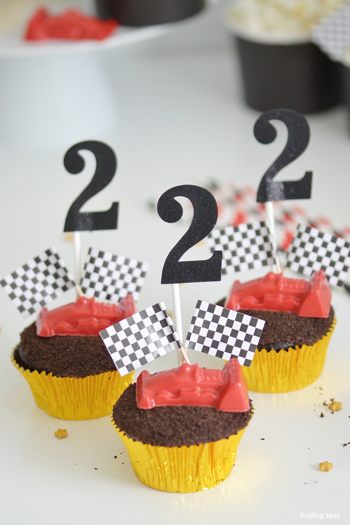 Ces deux cupcakes d'anniversaire rapides réaliseront les rêves de voiture de course de votre enfant.  Des cupcakes au chocolat garnis de voitures de course comestibles, de terre Oreo et de drapeaux à damiers.  Assurez-vous d'être un succès lors de votre fête d'anniversaire de course !