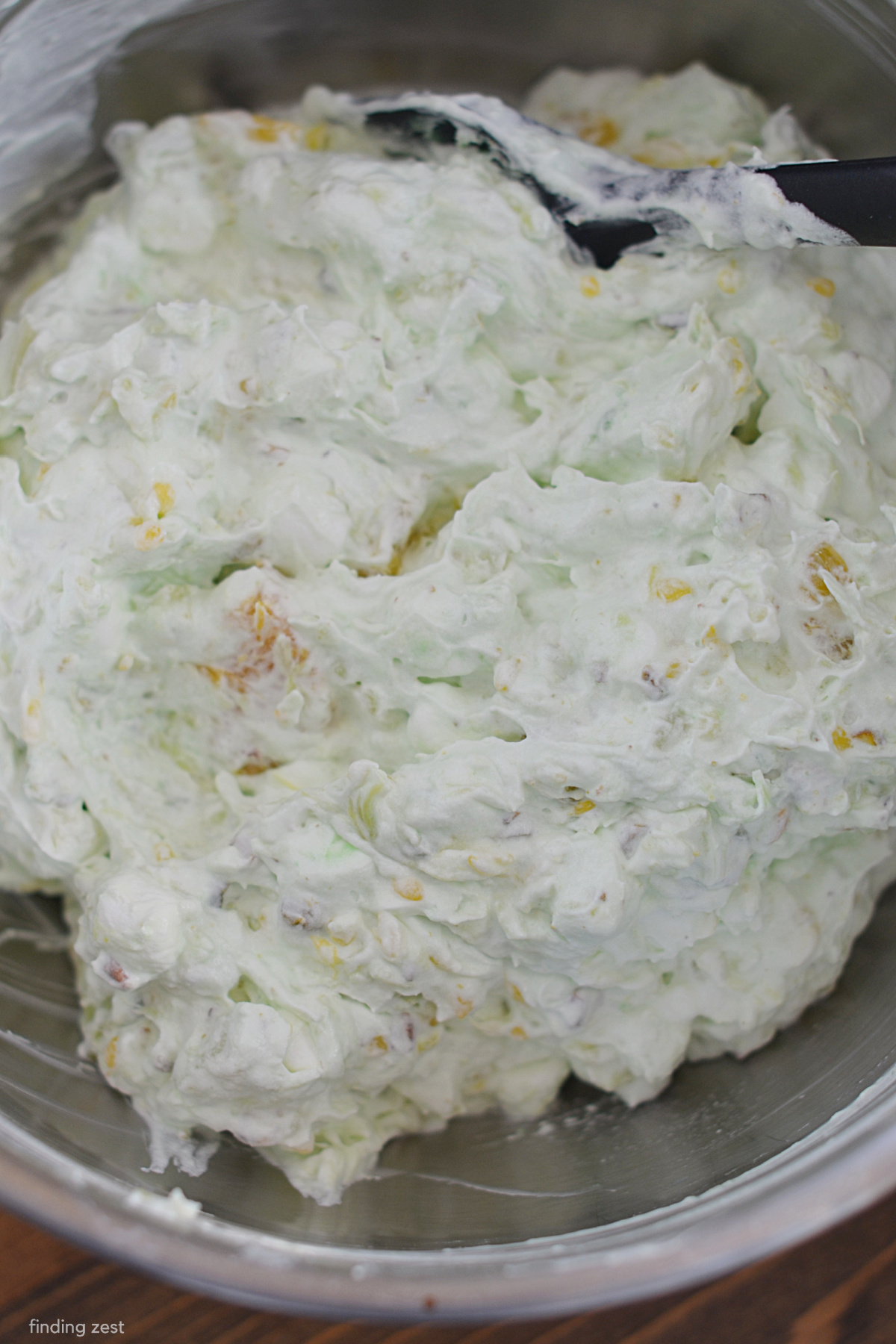 Mixing together ingredients for fluff with pistachio pudding, crushed pineapple, mini marshmallows and cool whip.