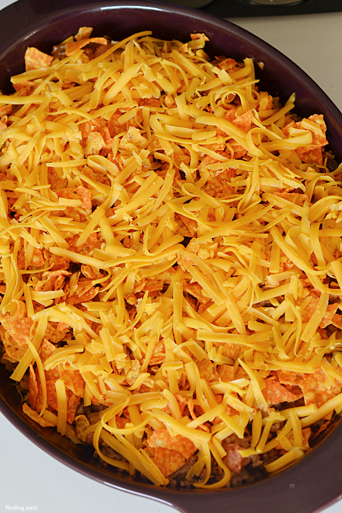 Topping a walking taco casserole with doritos and shredded cheese.