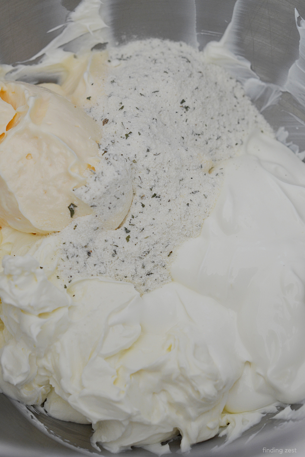 Making ranch veggie dip with Hidden Valley Ranch, sour cream, cream cheese and mayo in a bowl.