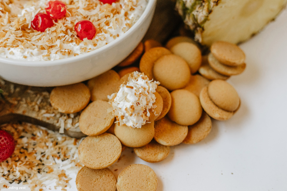 Tropical Pina Colada fruit dip served with strawberries and Nilla wafers, featuring a pineapple crown centerpiece and toasted coconut topping.